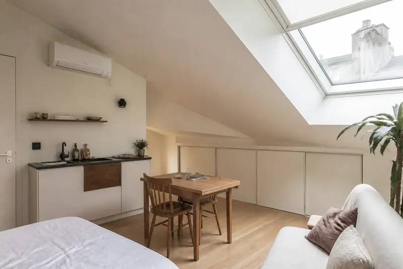 Petit studio sous toiture avec un climatiseur mural blanc installé près du plafond